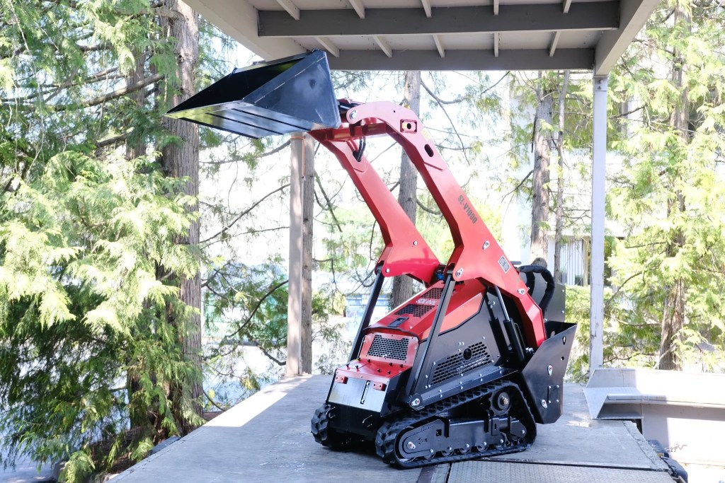 Rear three-quarter view of the SDLOOL SL-V1000 compact tracked mini skid steer with the loader arms raised to maximum hinge height.